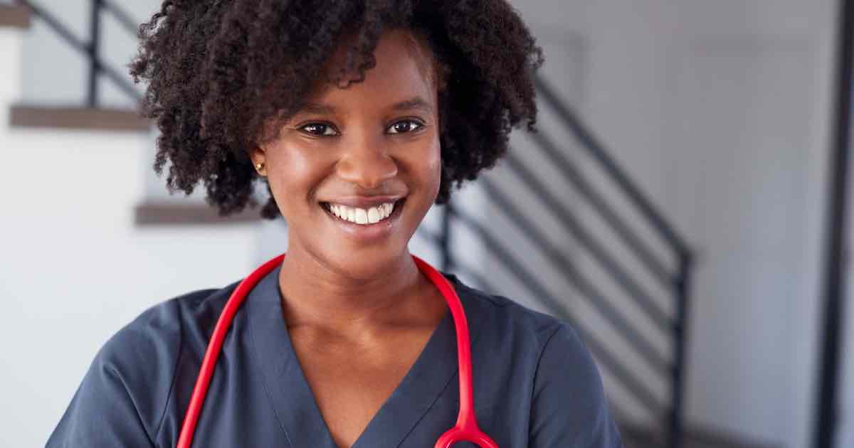 Young smiling female Black nurse in scrubs wearing red stethoscope around her neck conducting STD testing near me.
