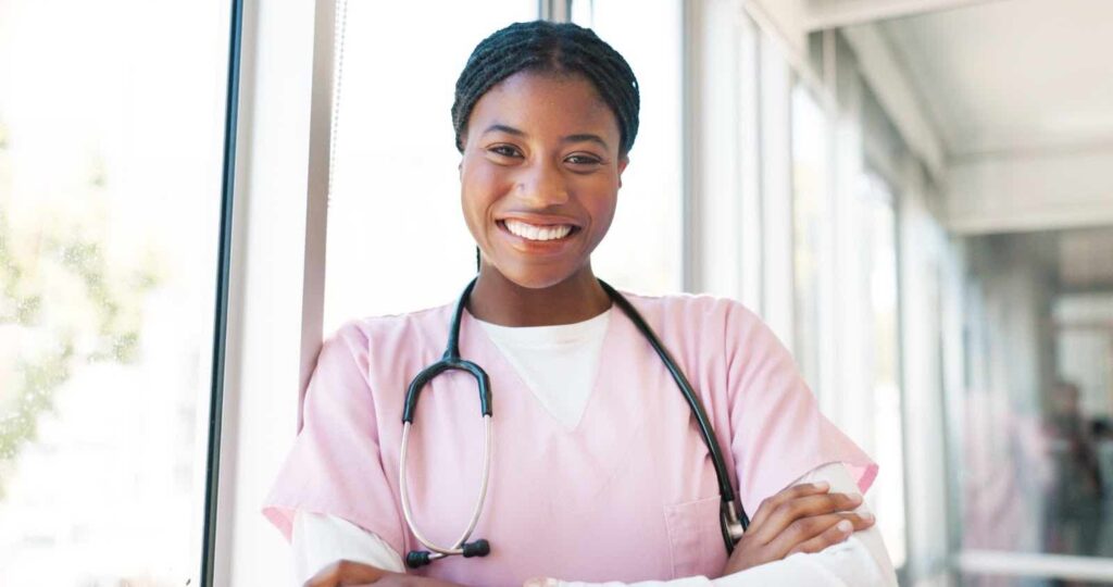 Smiling-Black-nurse-wearing-pink-scrubs-with-her-arms-crossed-in-a-relaxed-pose-from-a-womens-clinic-near-me