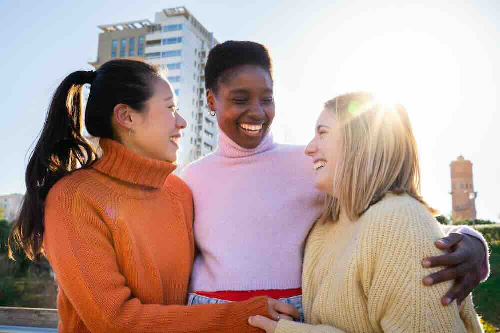 Three diverse friends laughing outside who know the answer to “what are common symptoms of STDs?”