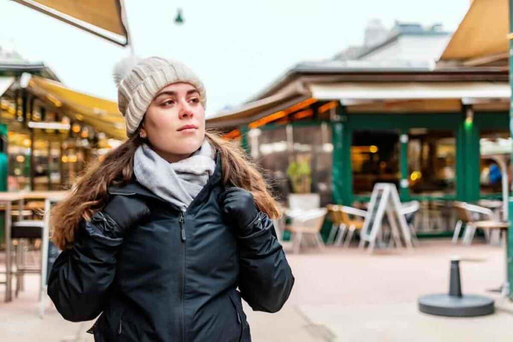 Woman in a beanie and leather jacket walking by an outdoor cafe while researching where is the easiest place to get tested for STDs.